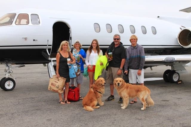 Travelers with luggage and dogs beside a private aircraft