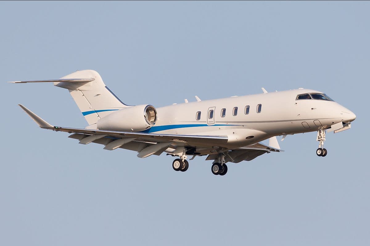 White super-midsize jet in flight with its landing gear extended