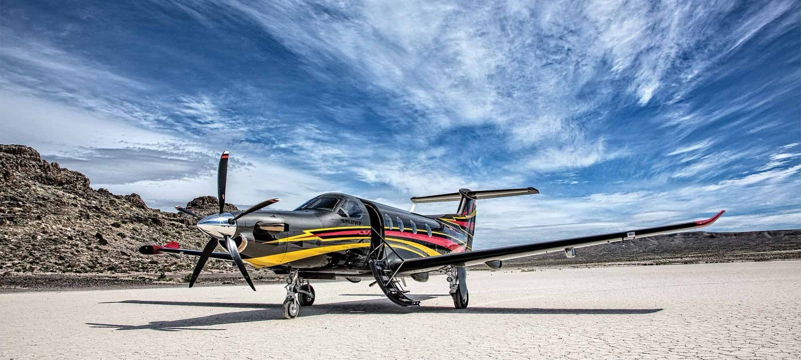 Single-engine turboprop parked with its boarding stairs open beside rocky terrain